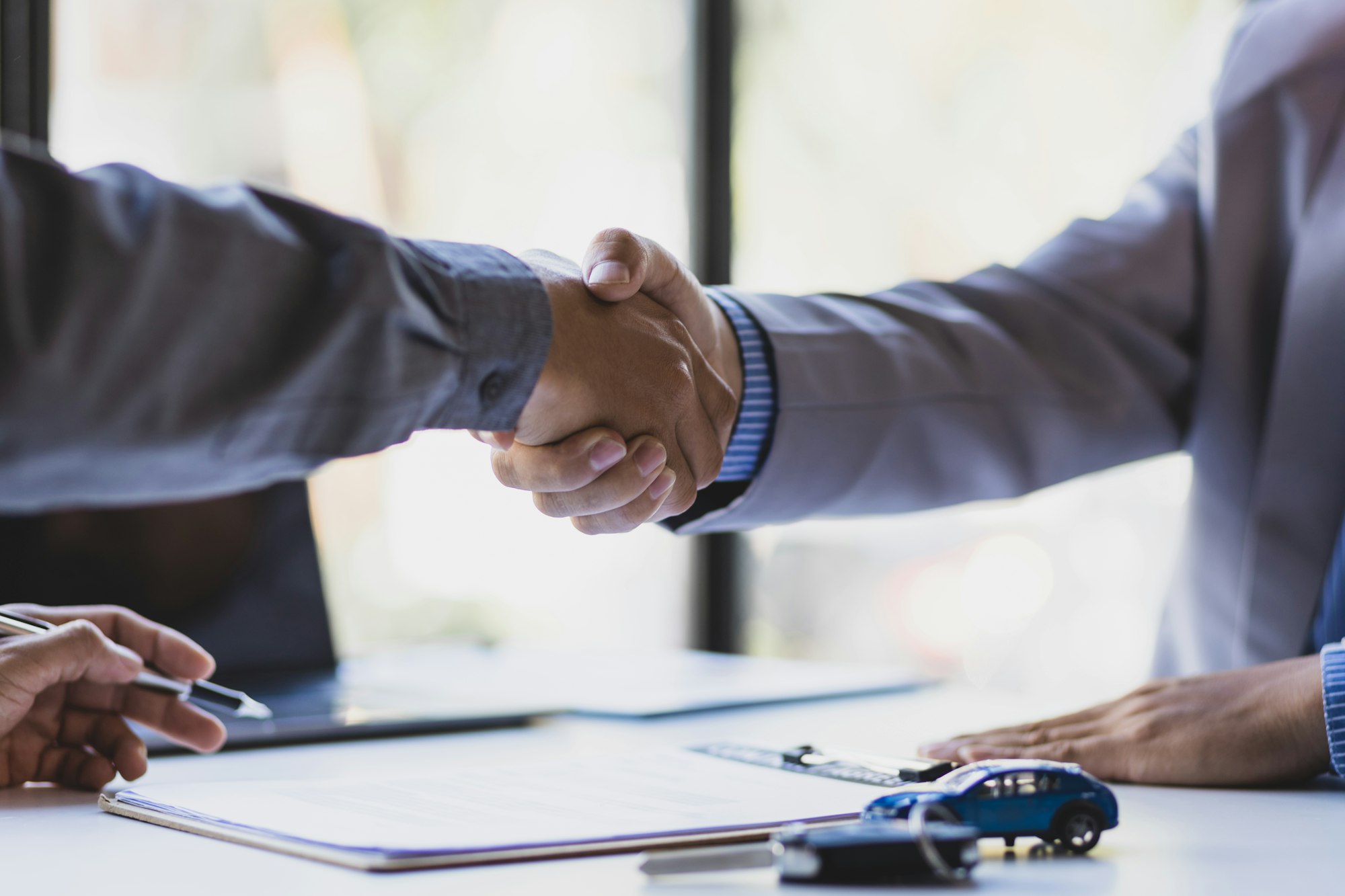 Businessmen shaking hands after signing a car sale with a car salesman.